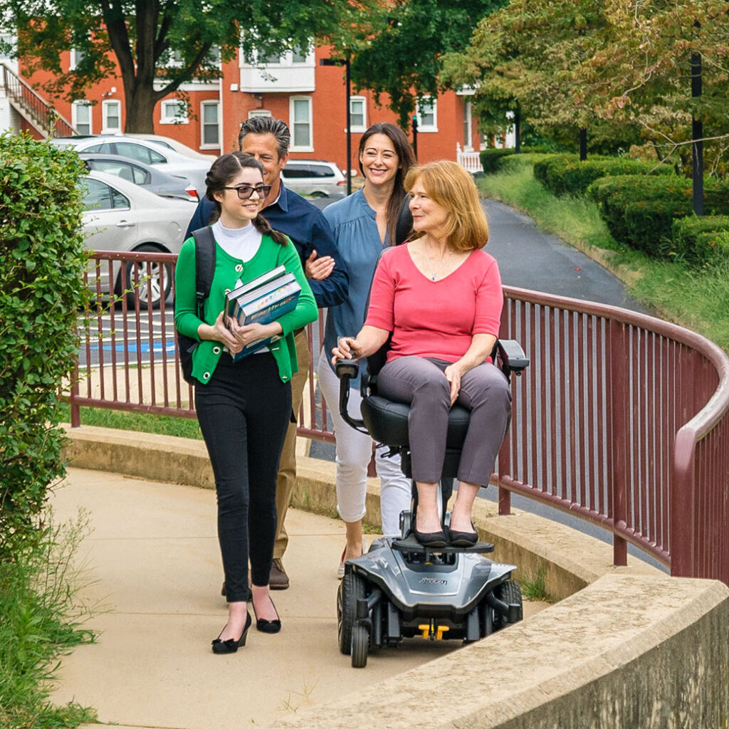 a woman riding a powerchair with people walking beside and behind her