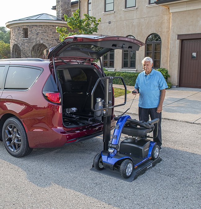 A man using a vehicle lift to get a mobility scooter into a mini van